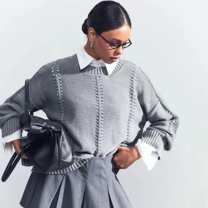 Woman wearing a gray sweater and skirt with a black handbag on a light gray background