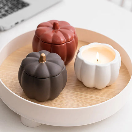 Three ceramic pumpkin-shaped containers on a wooden tray with a candle.