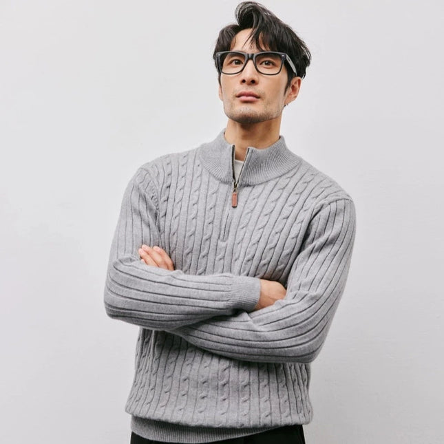 Man wearing a gray cable knit sweater with a plain background