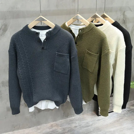 Four sweaters in different colors hanging on a rack against a gray wall.