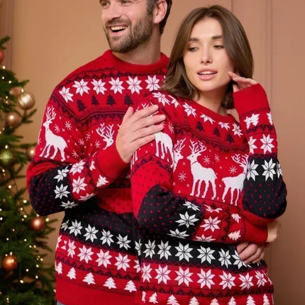 Two people wearing matching red Christmas sweaters with reindeer and snowflake patterns in front of a decorated Christmas tree.