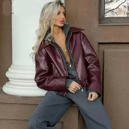 Woman wearing a maroon leather jacket sitting against a building.